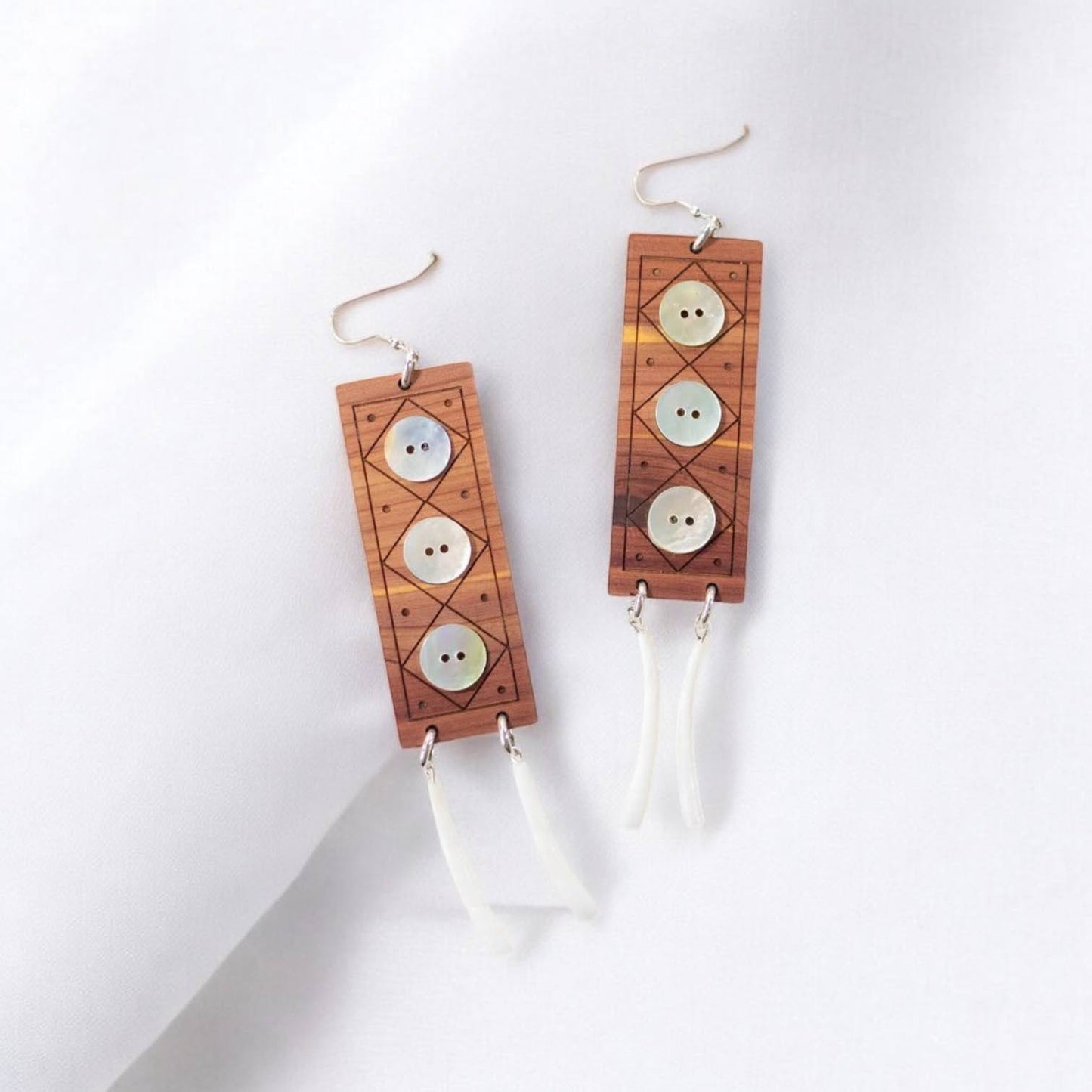 A pair of "Echoes of Celebration" earrings from Copper Canoe Woman laying on white fabric.