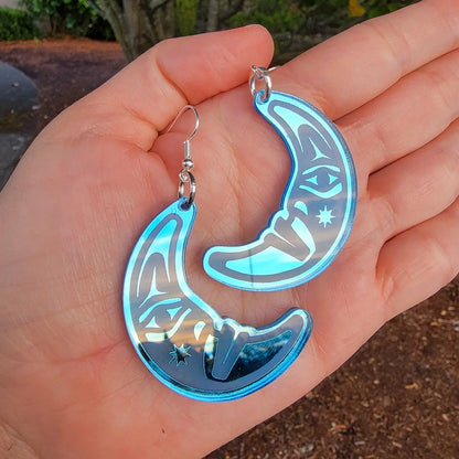 hand holding sky blue acrylic crescent moon engraved with formline art from copper canoe woman