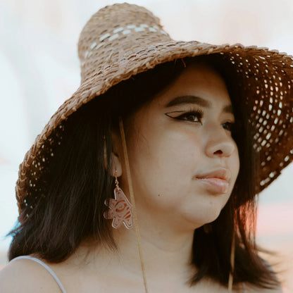 A model wearing a cedar hat and rose gold mirror acrylic "Balance Sun" earrings from Copper Canoe Woman.