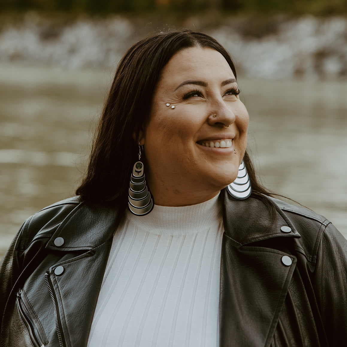 A smiling model wears the "Coastal Strata" earring in silver mirror acrylic, by Copper Canoe Woman.