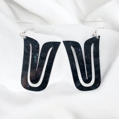 A pair of black acrylic "Echoed U" earrings on white fabric.