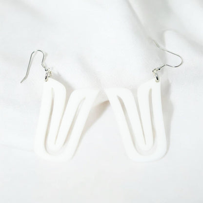 A pair of white acrylic "Echoed U" earrings resting on white fabric.