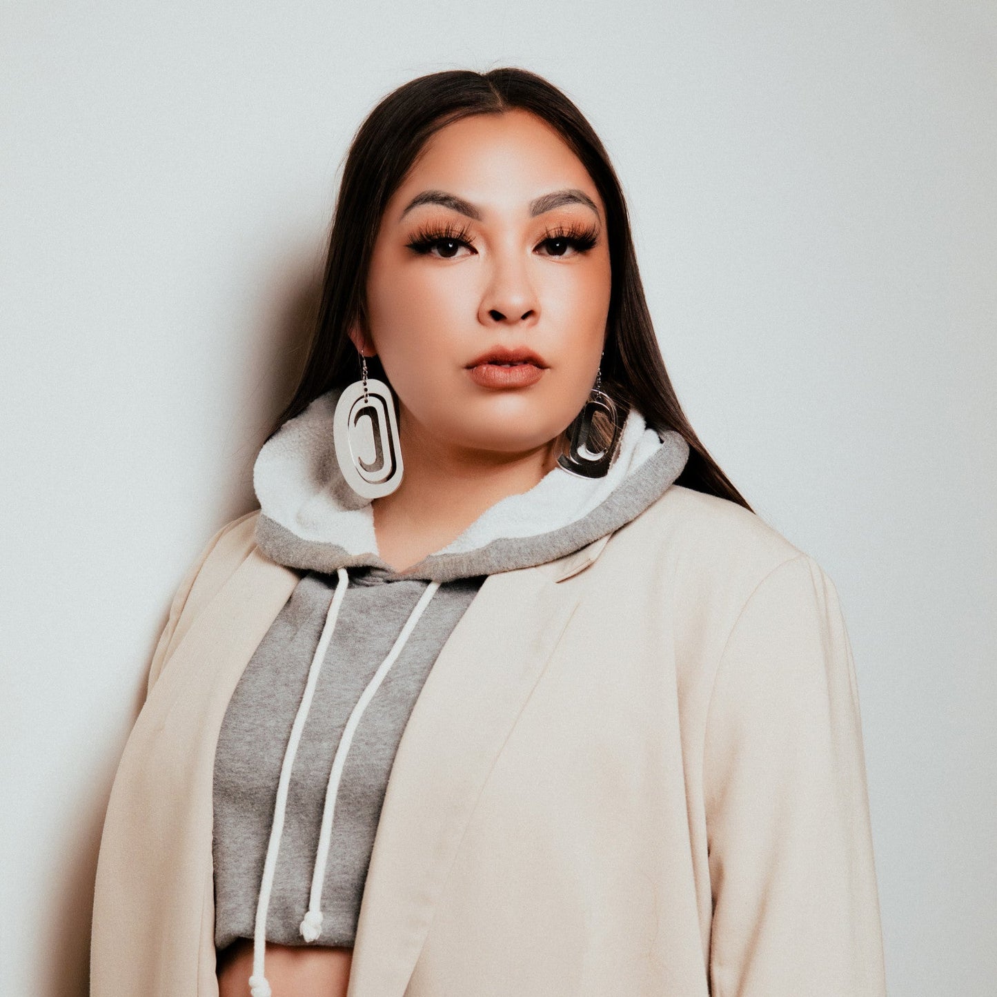 A person wearing rhodium platinum large ovoid earrings from Copper Canoe Woman with a grey hoodie and a beige coat.