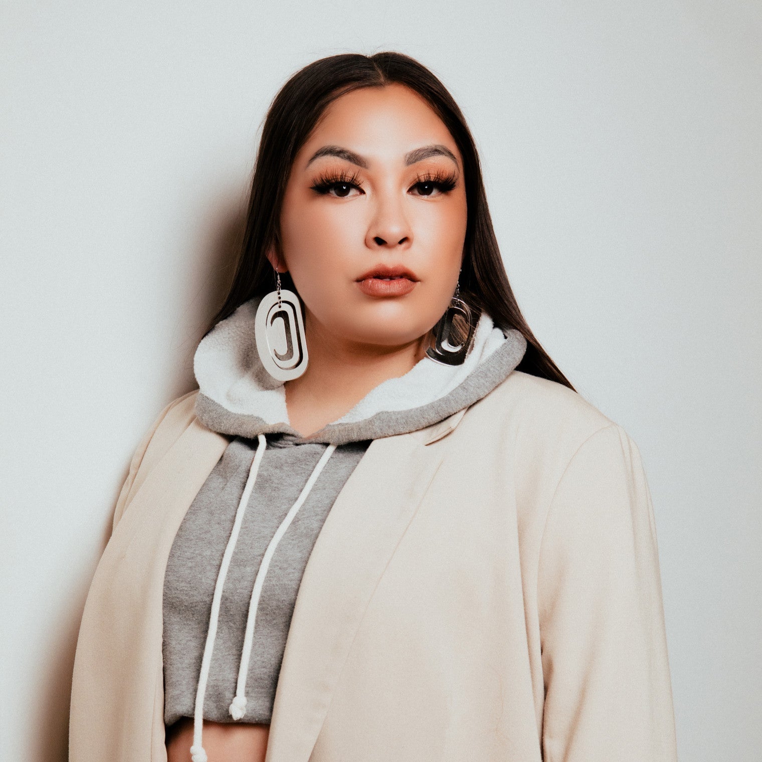 A person wearing rhodium platinum large ovoid earrings from Copper Canoe Woman with a grey hoodie and a beige coat.