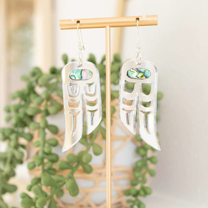 A pair of silver mirror acrylic "Love Birds" earrings from Copper Canoe Woman hang from a display stand.