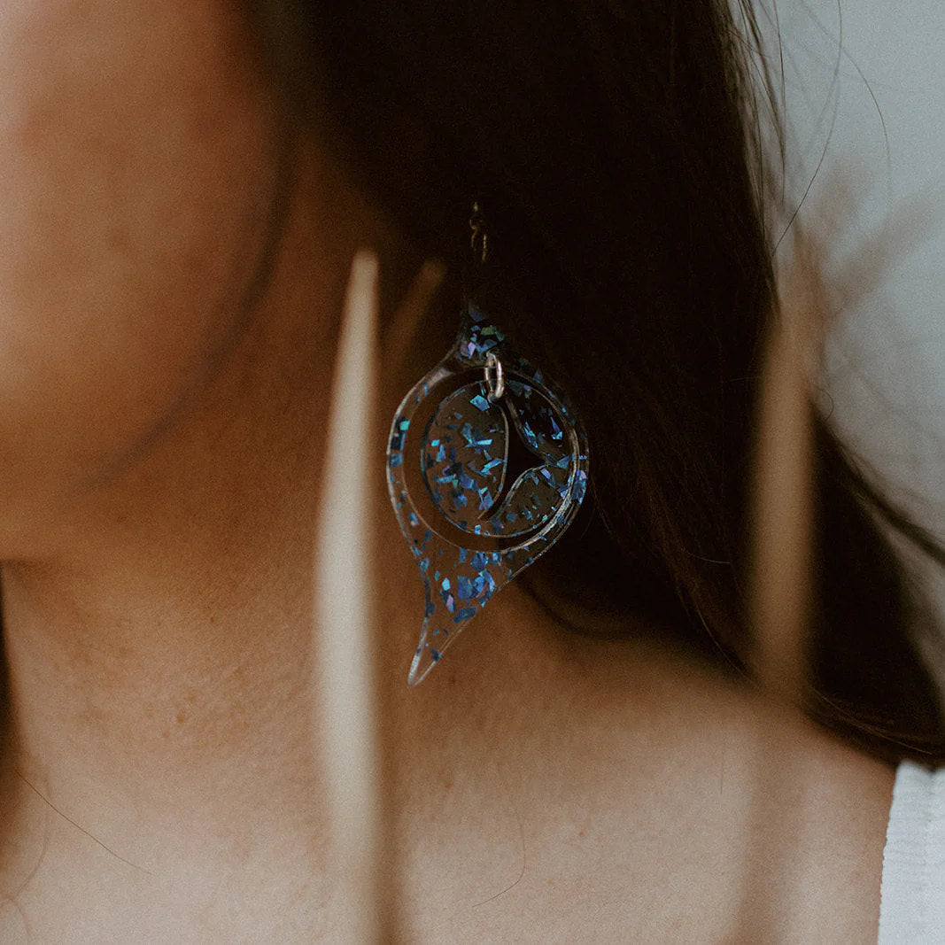 A closeup of a woman wearing blue flake acrylic "Octopus Eye" earrings from Copper Canoe Woman.