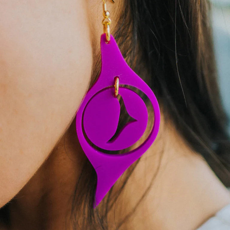 A closeup of a model wearing an electric grape acrylic "Octopus Eye" earring from Copper Canoe Woman.