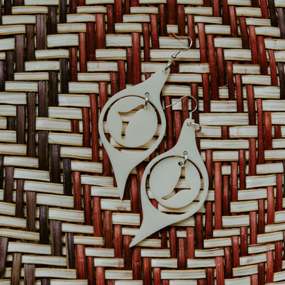 A pair of "Octopus Eye" earrings in ivory acrylic laying on a woven mat.