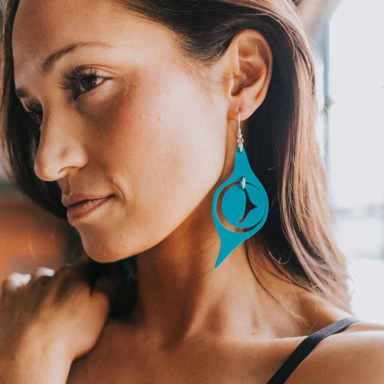 A model wearing an "Octopus Eye" earring in lagoon blue acrylic from Copper Canoe Woman.