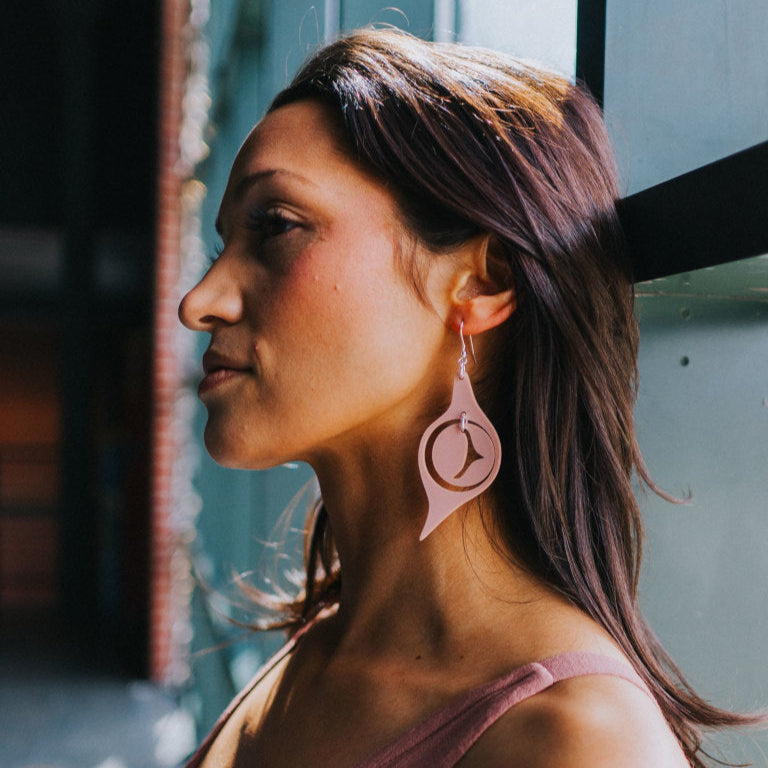 A model leans against a window wearing matte blush acrylic "Octopus Eye" earrings from Copper Canoe Woman.