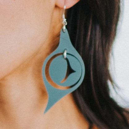 Closeup of a woman wearing a matte sage acrylic "Octopus Eye" earring from Copper Canoe Woman.