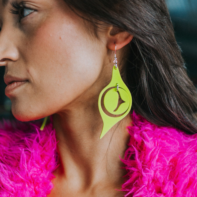 A model wears a pair of "Octopus Eye" earrings in neon pear acrylic from Copper Canoe Woman.