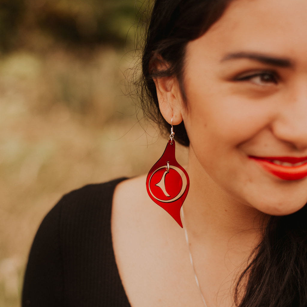 A model in a field wearing red acrylic "Octopus Eye" earrings from Copper Canoe Woman.