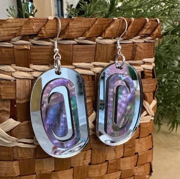 A pair of silver mirror acrylic "Abalone Ovoid" earrings from Copper Canoe Woman hang from a basket.