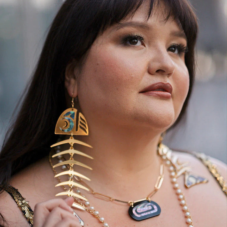 A model wearing gold mirror acrylic large salmon ghost earrings from Copper Canoe Woman.