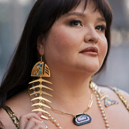 A model wearing gold mirror acrylic large salmon ghost earrings from Copper Canoe Woman.