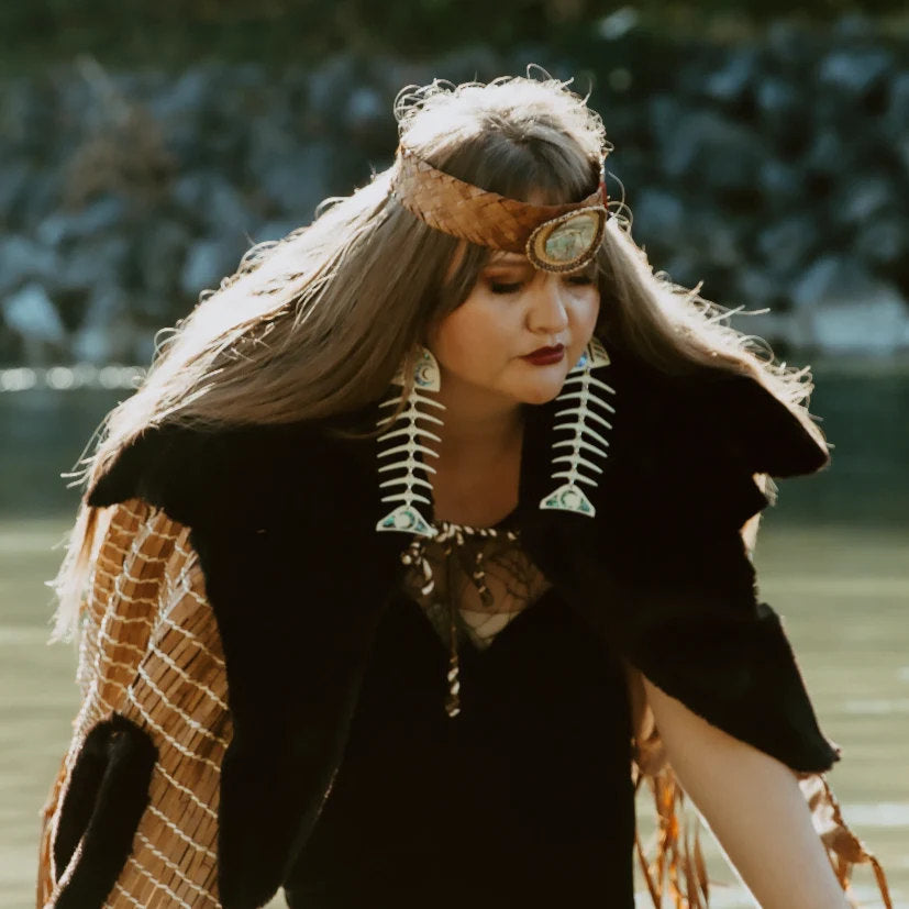 A model wearing Indigenous regalia and large salmon ghost earrings in ivory acrylic from Copper Canoe Woman.