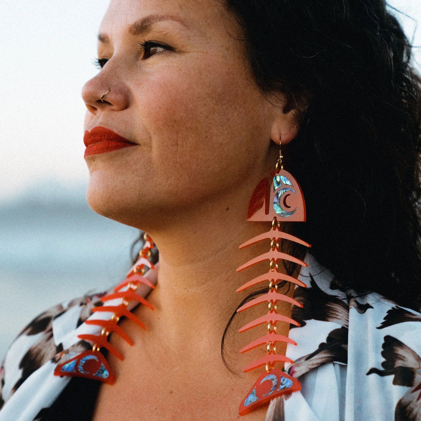A model in profile wearing red acrylic large salmon ghost earrings from Copper Canoe Woman.