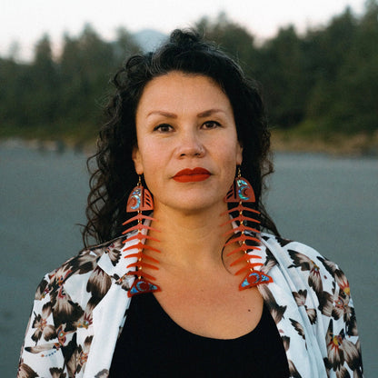 Model stares at camera while wearing large salmon ghost earrings in red acrylic from Copper Canoe Woman.