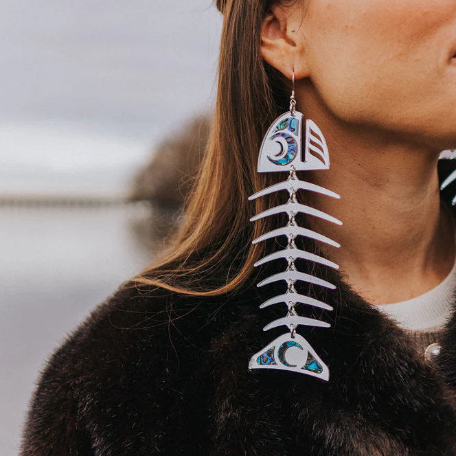 Closeup of a model wearing large salmon ghost earrings in silver mirror acrylic from Copper Canoe Woman.