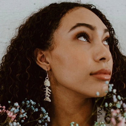 A woman looking upward showcases the ivory acrylic small salmon ghost earring from Copper Canoe Woman.