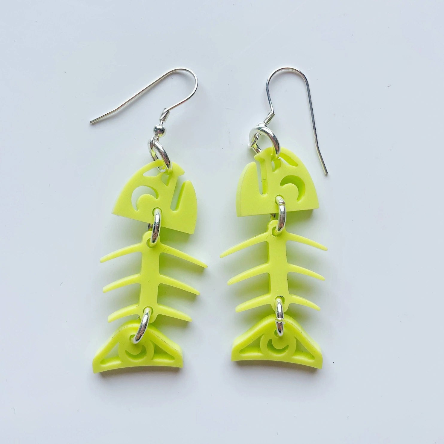 A pair of neon pear acrylic small salmon ghost earrings from Copper Canoe Woman laying on a white background.
