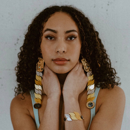 Model stares into the camera wearing yellow and gold mirror acrylic serpent earrings from Copper Canoe Woman.