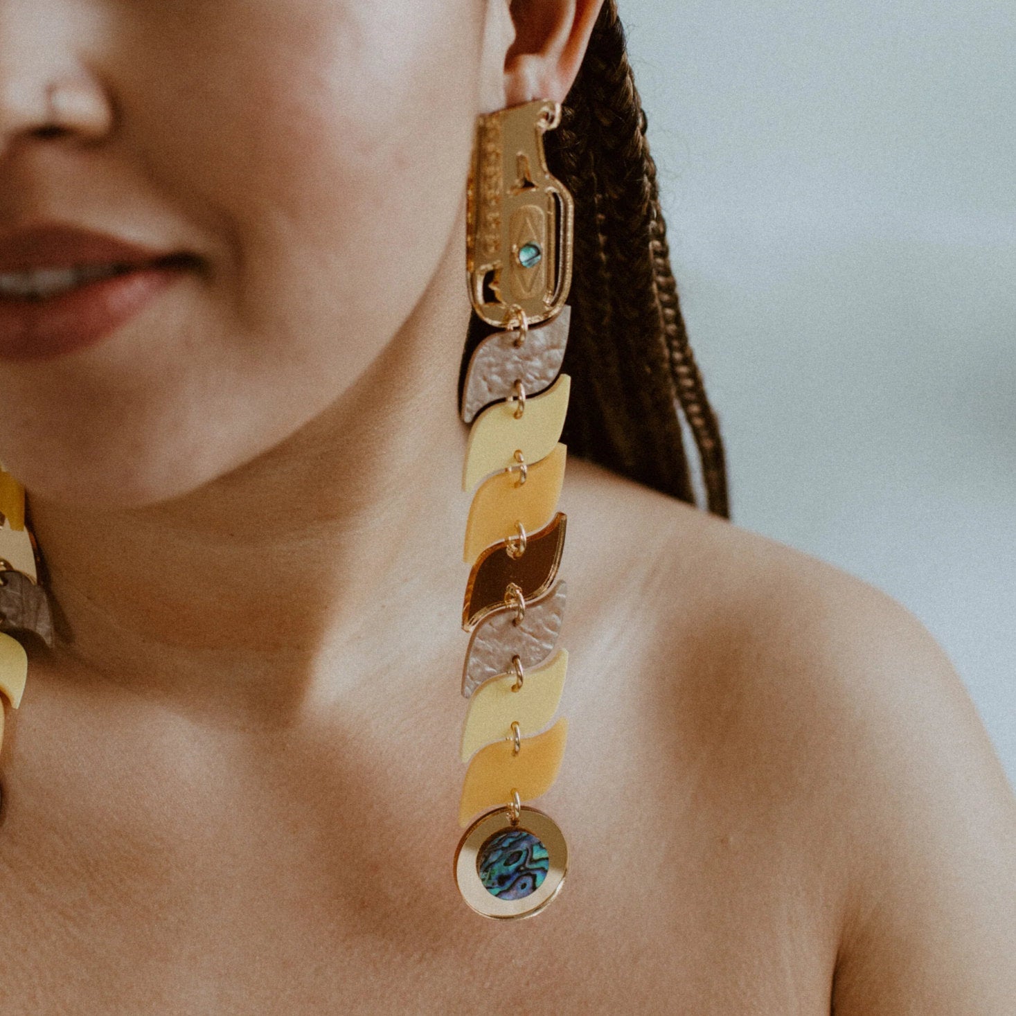 Closeup of a model wearing yellow and gold mirror acrylic serpent earrings from Copper Canoe Woman.