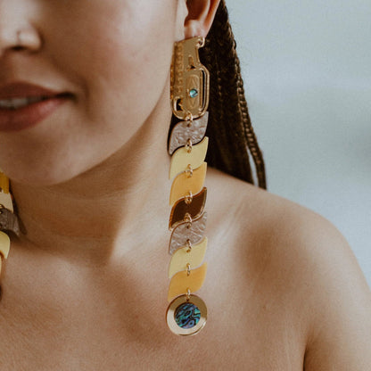 Closeup of a model wearing yellow and gold mirror acrylic serpent earrings from Copper Canoe Woman.