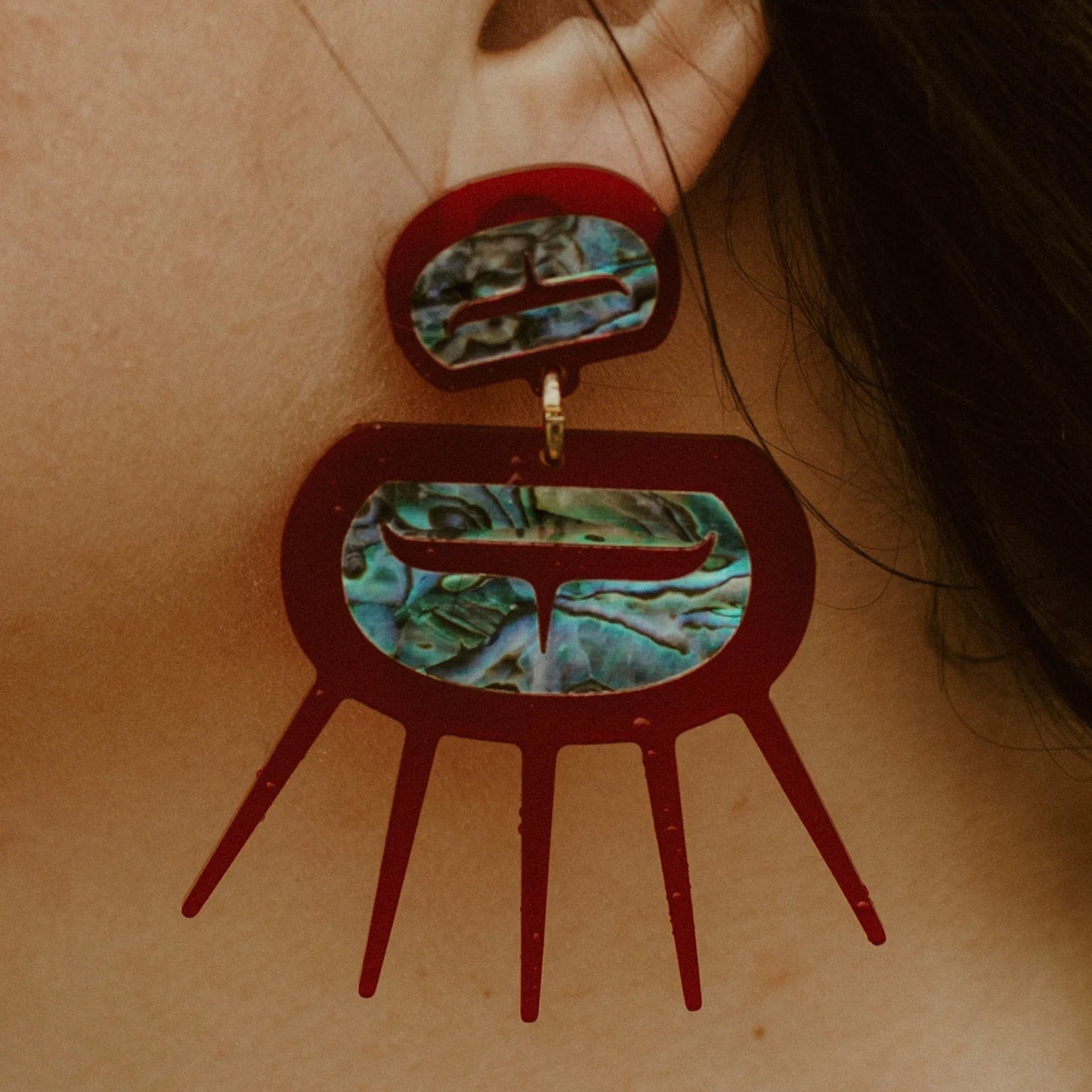 Closeup of a model wearing red translucent acrylic Urchin earrings from Copper Canoe Woman.