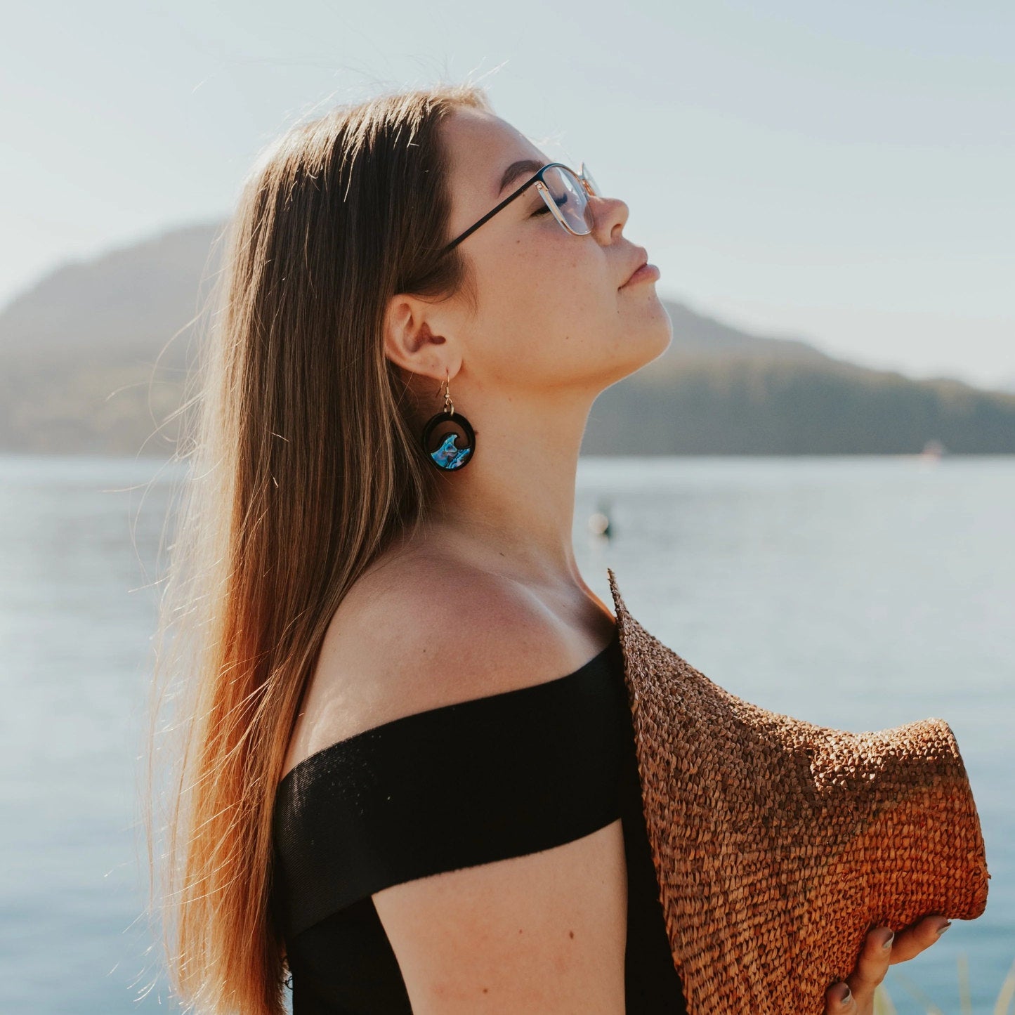 young woman wearing black acrylic earring with wave cut out and abalone inlay from copper canoe woman